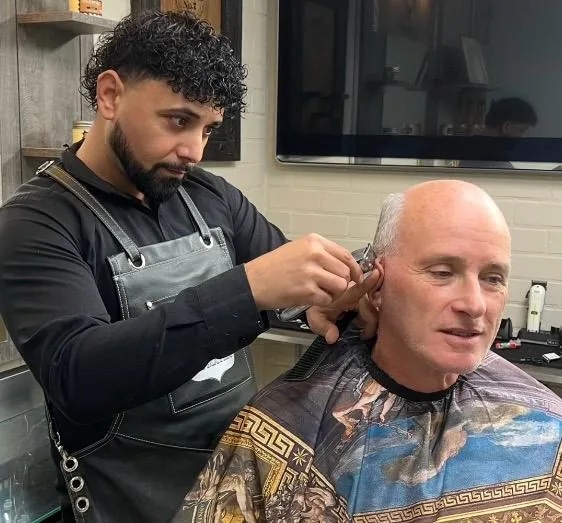 Barbier werkt het haar van een klant bij in Barbershop De Maten